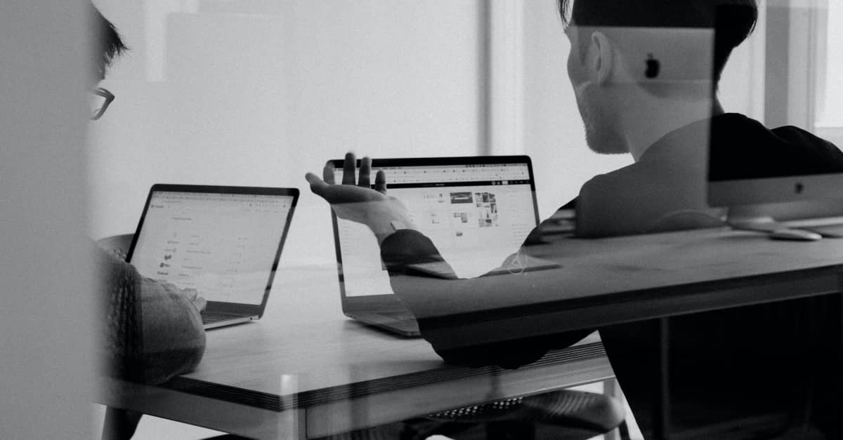 Two people working on laptops in a meeting room, viewed through glass