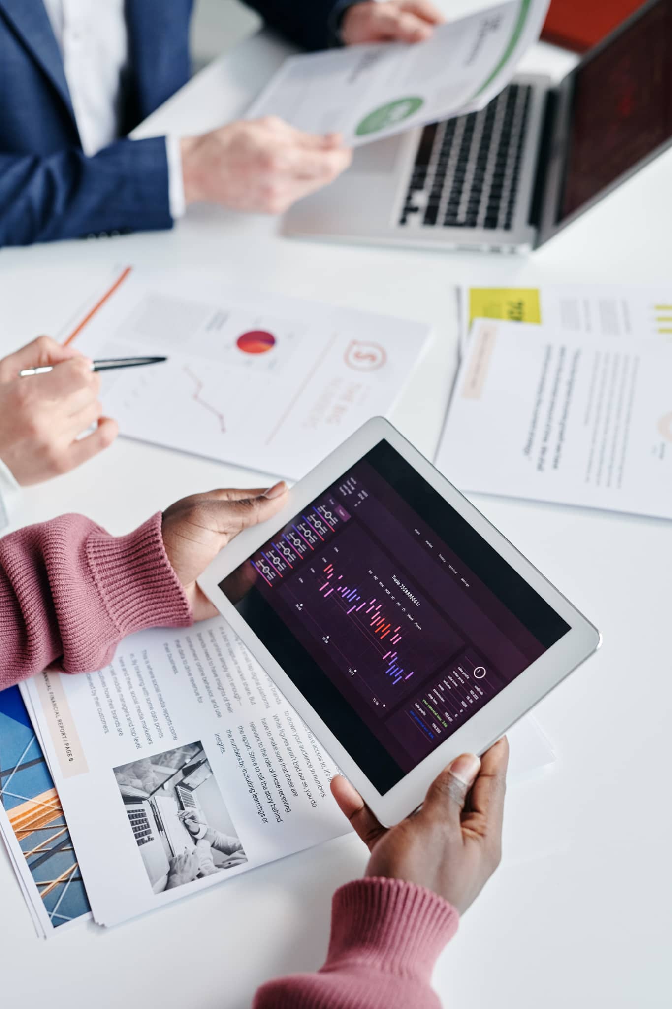 Two people reviewing charts and graphs on a tablet and printed documents at a desk.