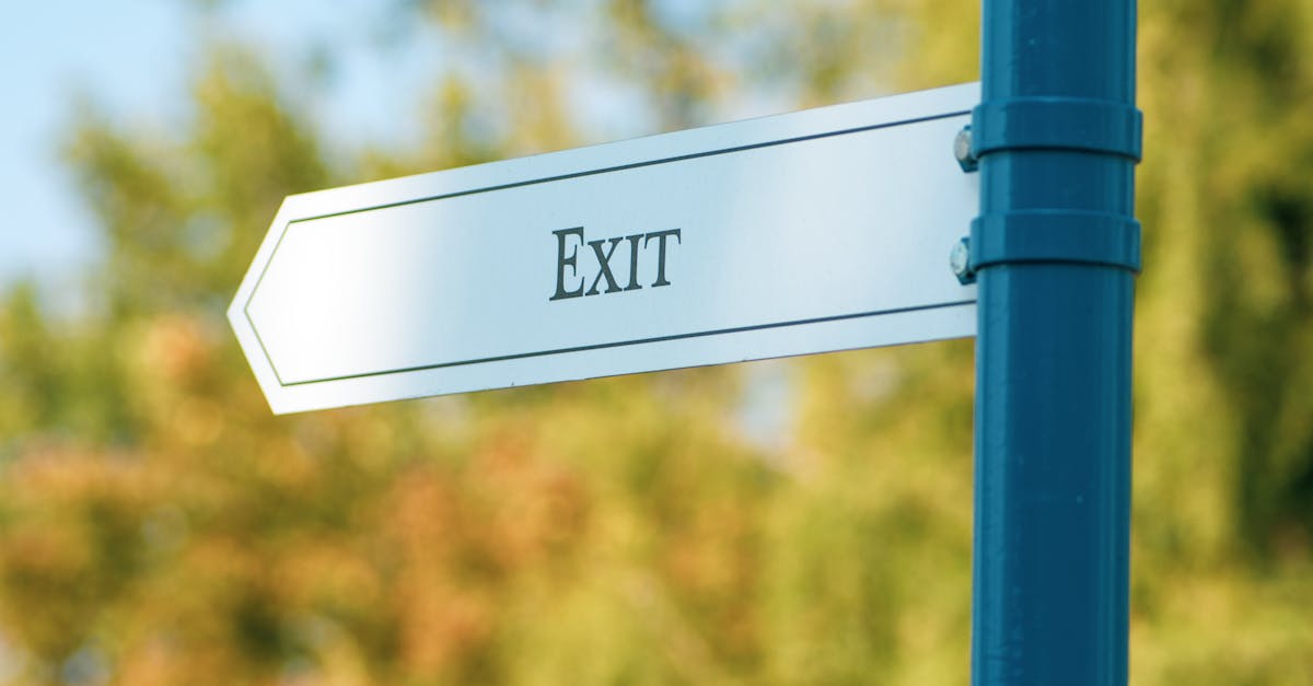 A close-up view of an exit sign mounted on a blue pole in a lush outdoor setting.