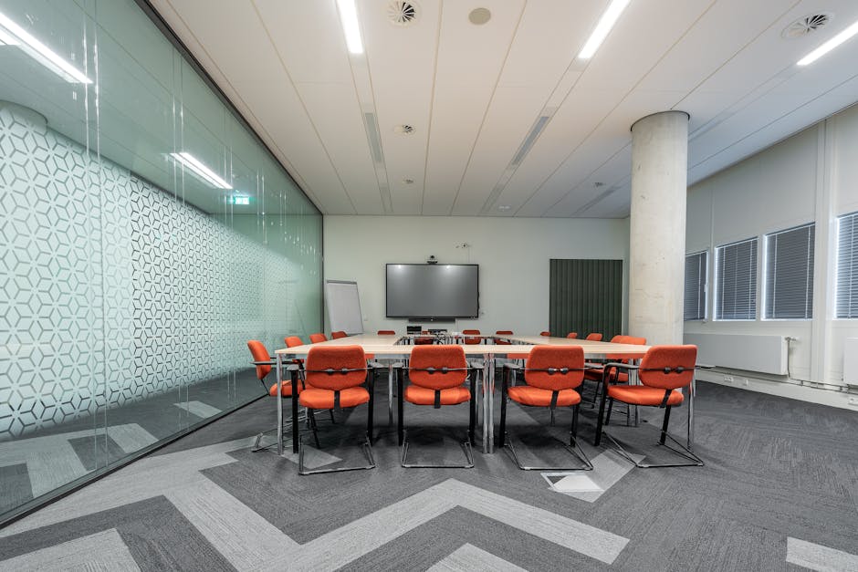 Spacious conference room with a large meeting table, red chairs, and glass walls for natural lighting.