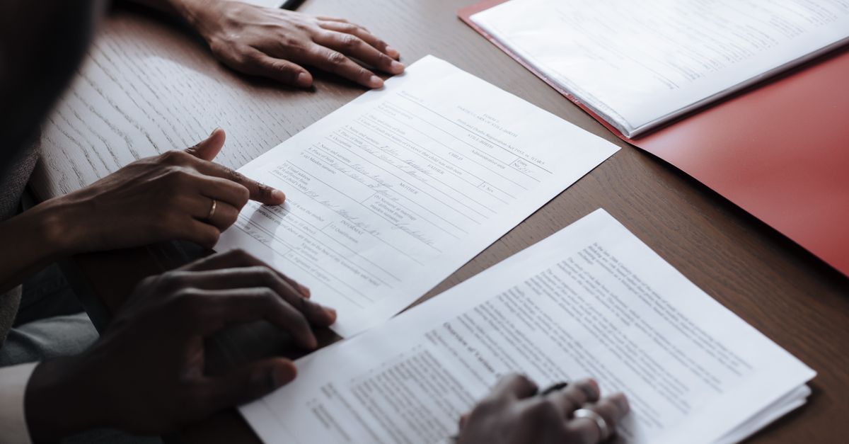 Two individuals reviewing and signing official documents in an indoor setting.