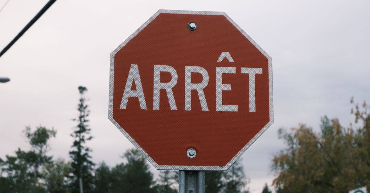 Close-up of a red French stop sign outdoors with trees in the background.