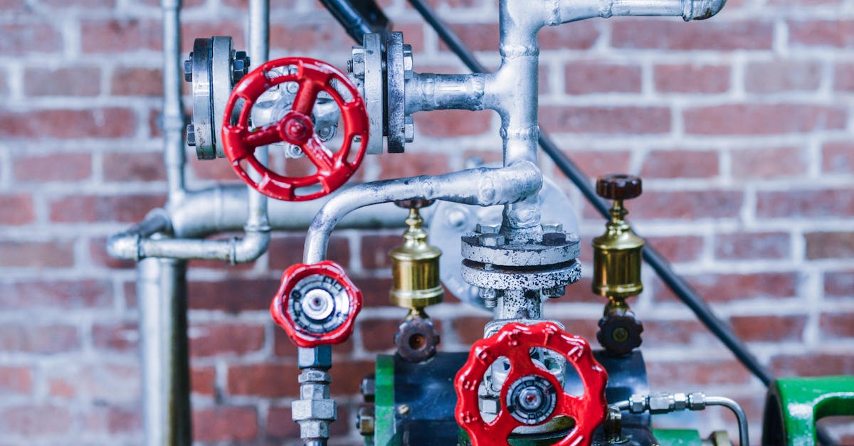 Close-up of industrial machinery with red valve handles and metal pipes against a brick wall.