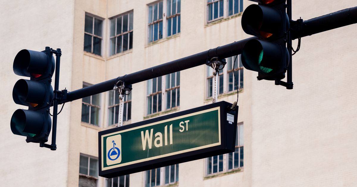 Traffic lights and Wall St sign in cityscape, symbolizing finance hub.