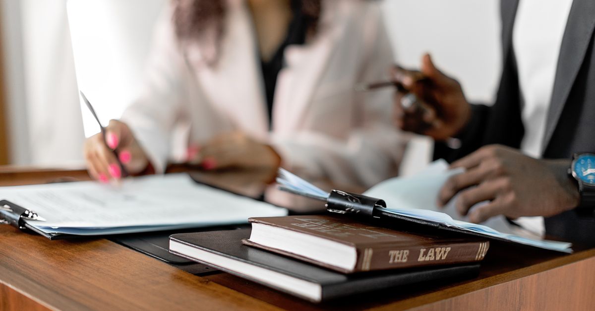 Two lawyers reviewing documents with law books on a desk. Professional legal environment.