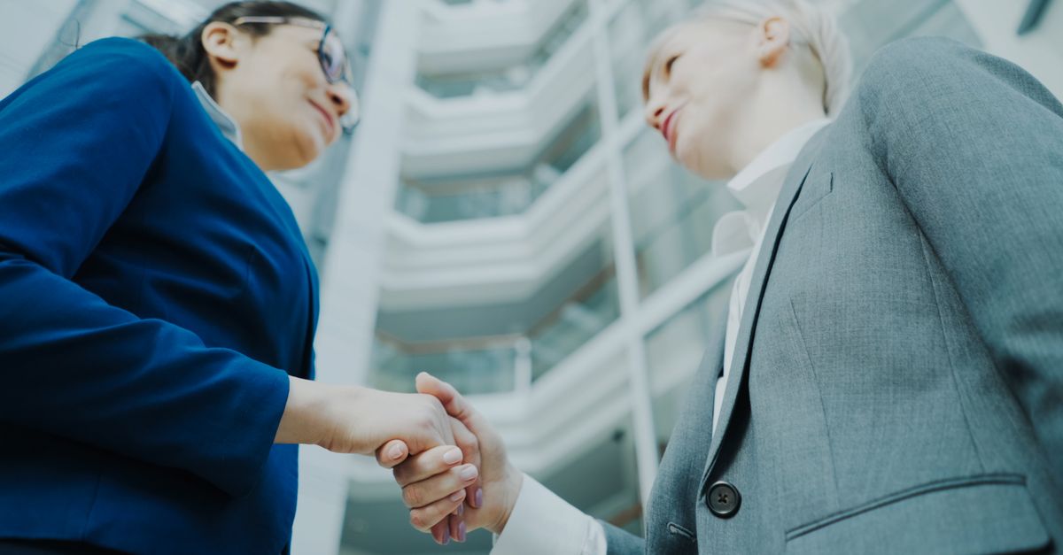 Two business professionals shaking hands in a modern office atrium, symbolizing collaboration.