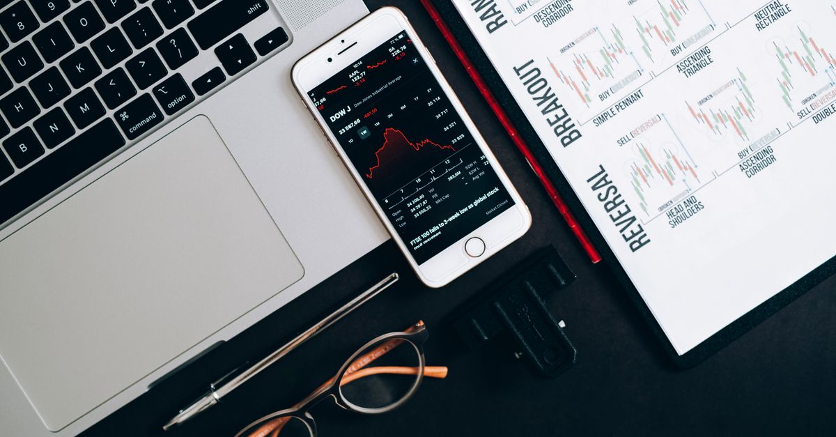 Top view of financial tools including a laptop, smartphone with stock data, and charts for market analysis.