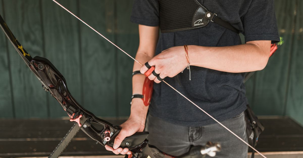 A focused archery athlete preparing a recurve bow for shooting outdoors.