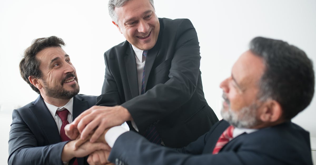 Three businessmen in suits celebrating teamwork success indoors with handshake.