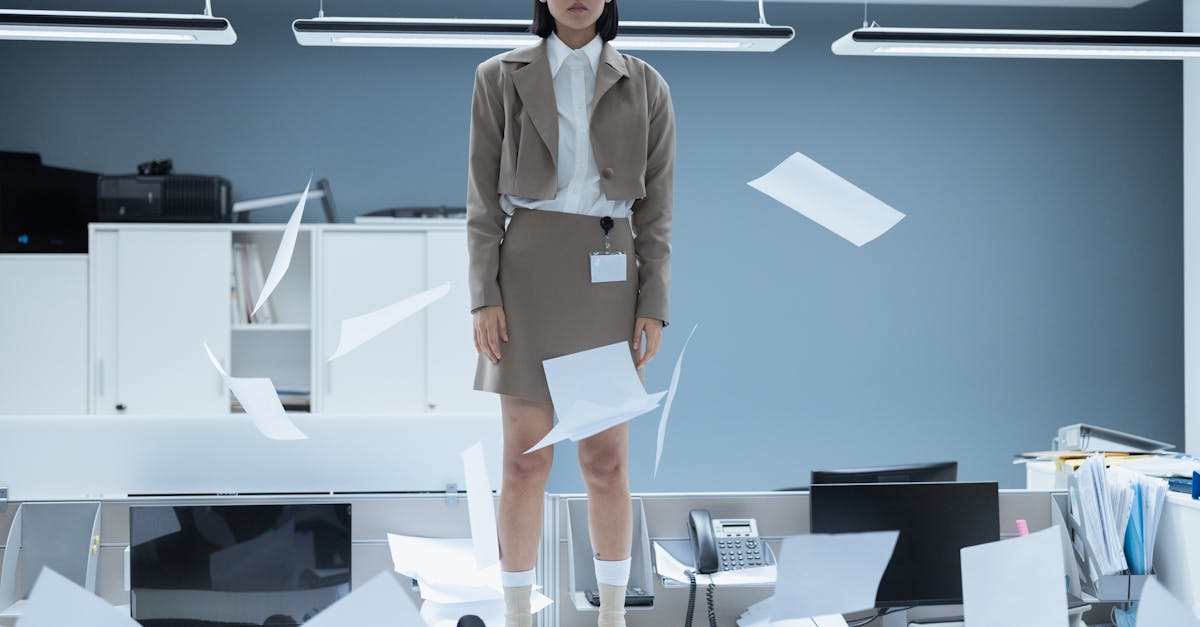 Fashionable young woman standing on a desk in a minimalist office with papers flying.