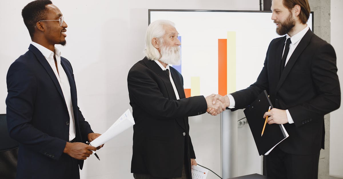 Three businessmen in suits having a meeting, shaking hands in front of a presentation chart.