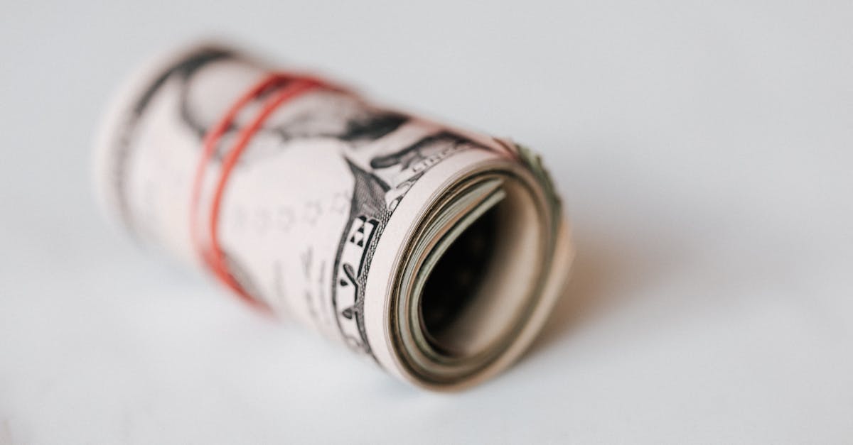 High angle roll of five dollar bills on white table tightened with red rubber band