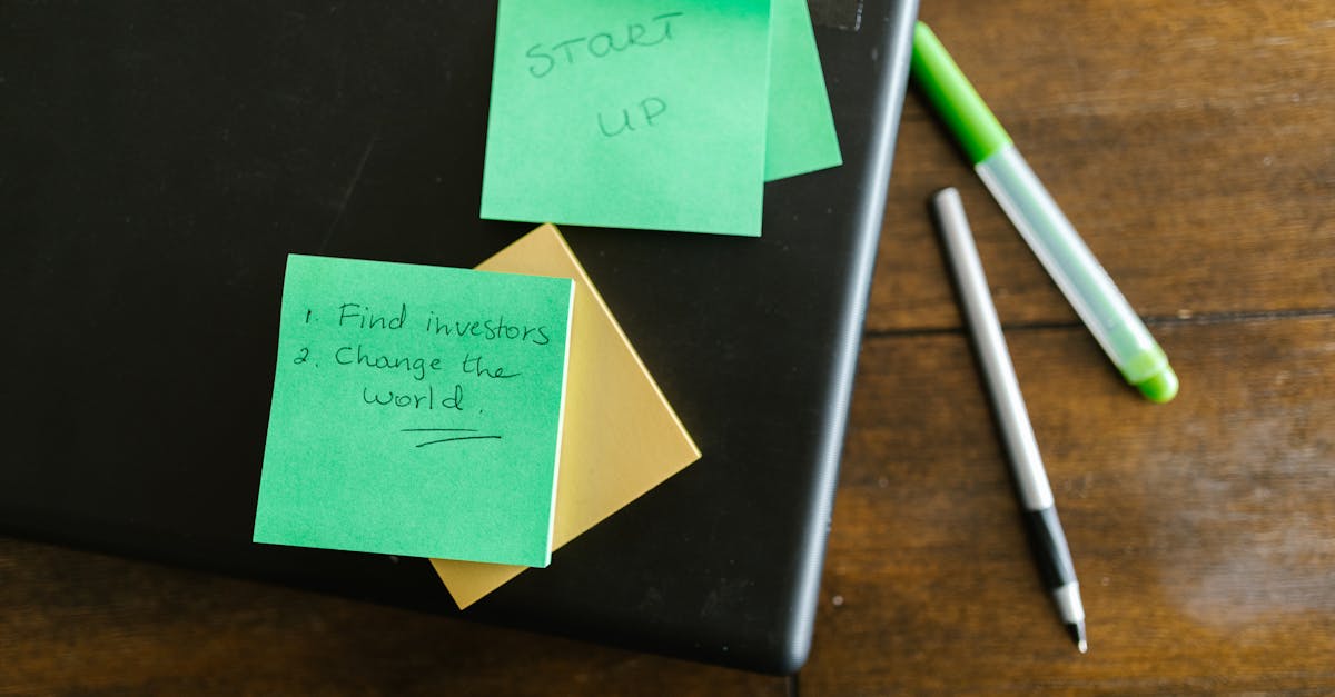 Green sticky notes with startup goals on a wooden desk with pens.