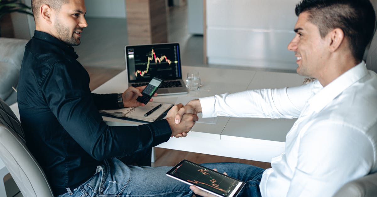 Two men shaking hands over a successful business deal with trading charts displayed.