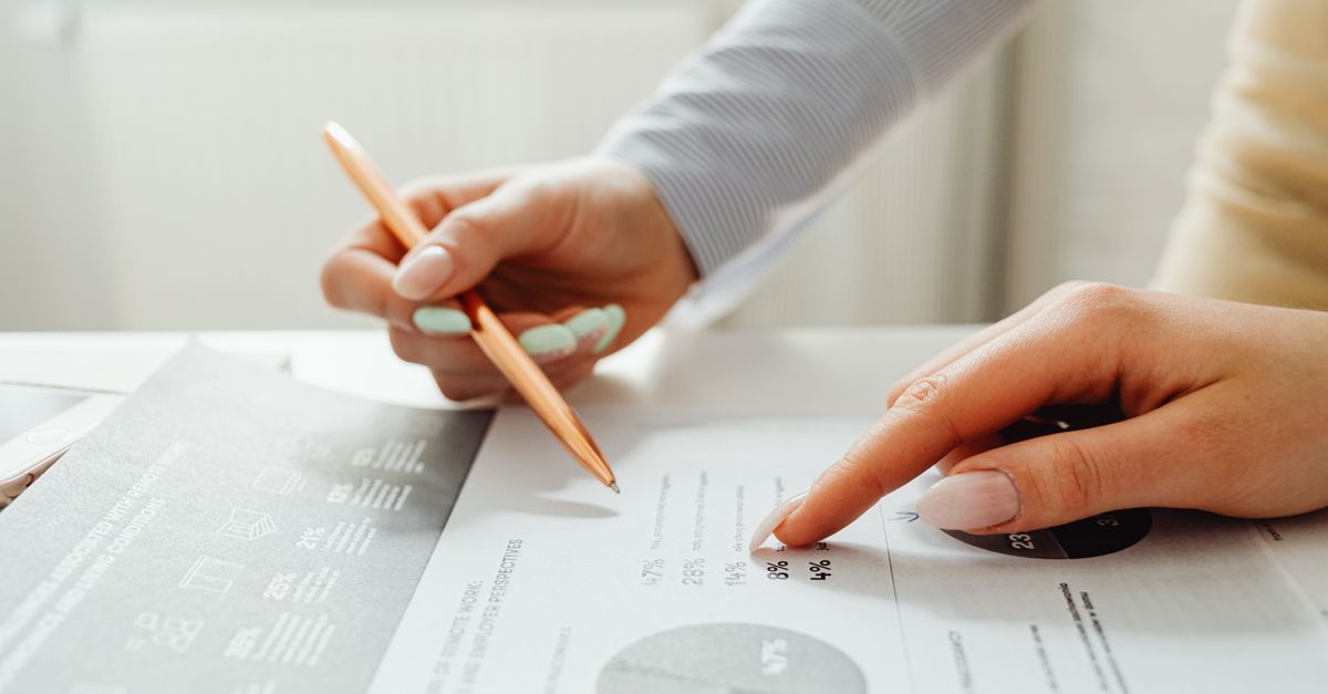 Hands holding a pencil, analyzing charts and data sheets, suggesting teamwork in an office setting.