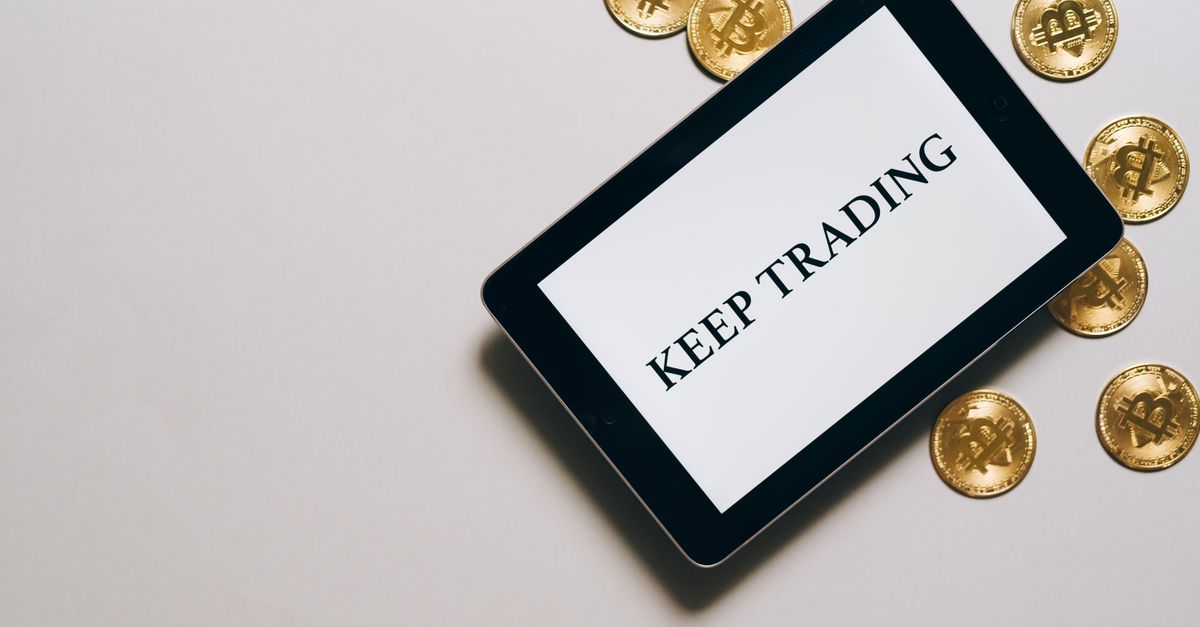 Tablet displaying 'Keep Trading' surrounded by Bitcoin coins on a white background, emphasizing digital currency and trading.