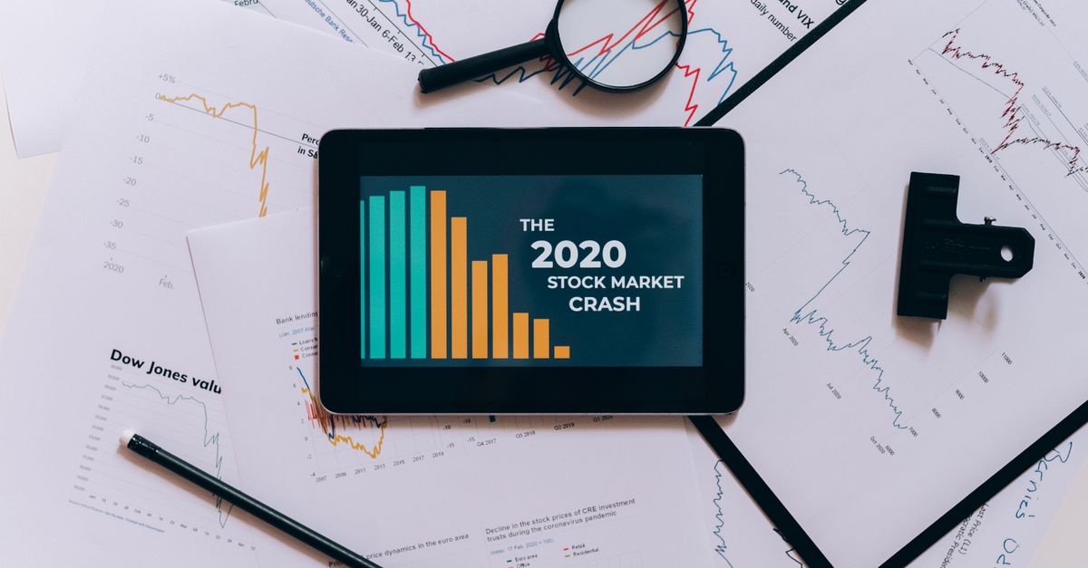 Flat lay of tablet showing 2020 stock market crash with charts and papers.