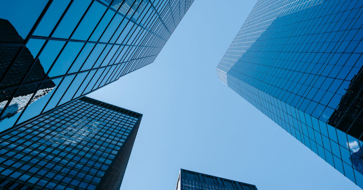 Upward angle of tall, glass skyscrapers with a clear blue sky, emphasizing modern architecture.