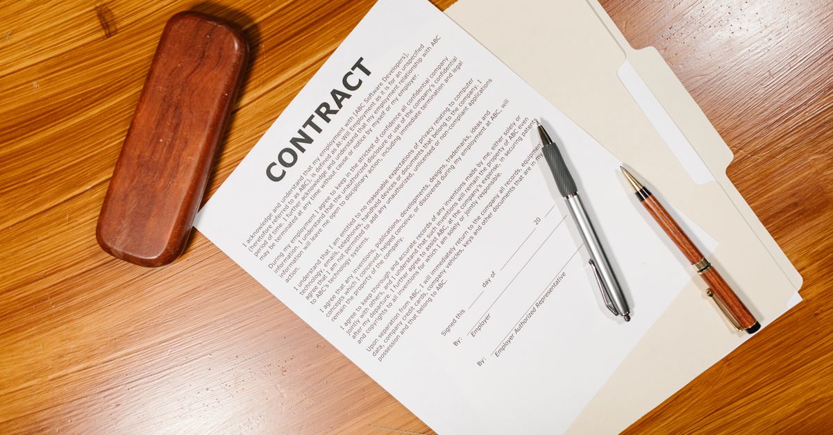 High-angle view of a contract document with pens and a case on a wooden table.
