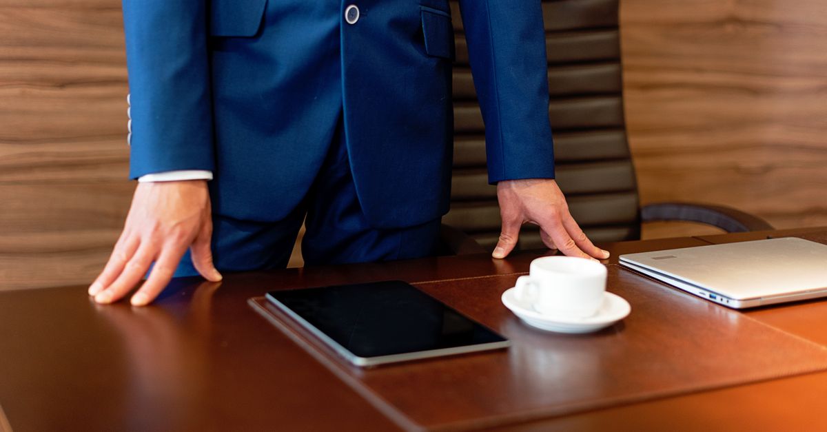 Professional businessman in blue suit standing by a desk with a tablet and coffee cup.