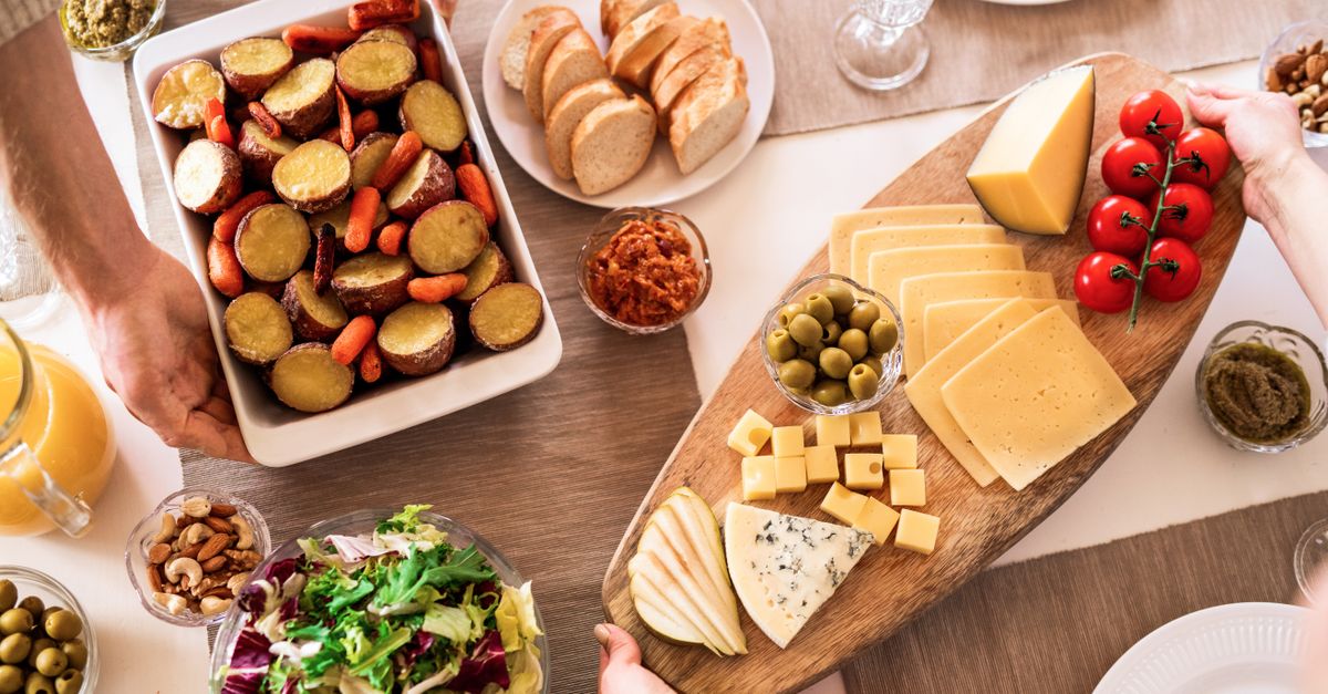 Delicious cheese platter with fresh vegetables, olives, and bread on a dining table.