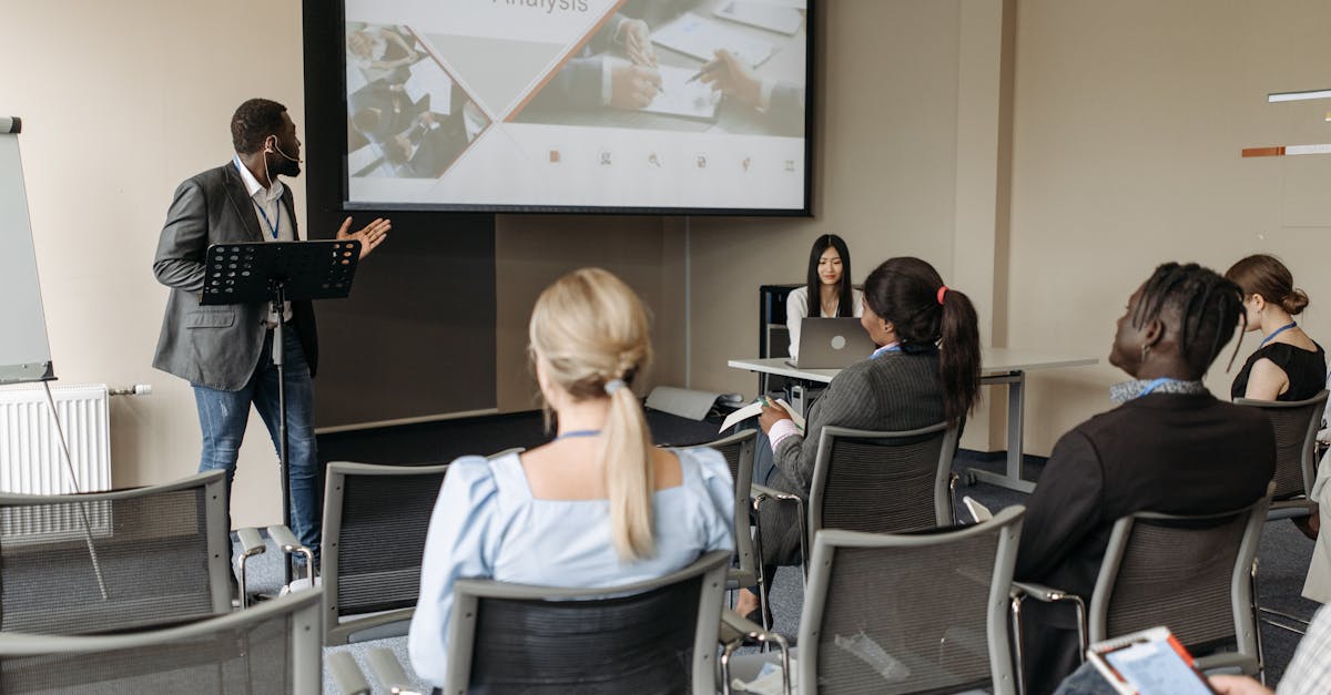 A diverse group attends a business analysis seminar with a presenter and projection screen in a modern conference room.