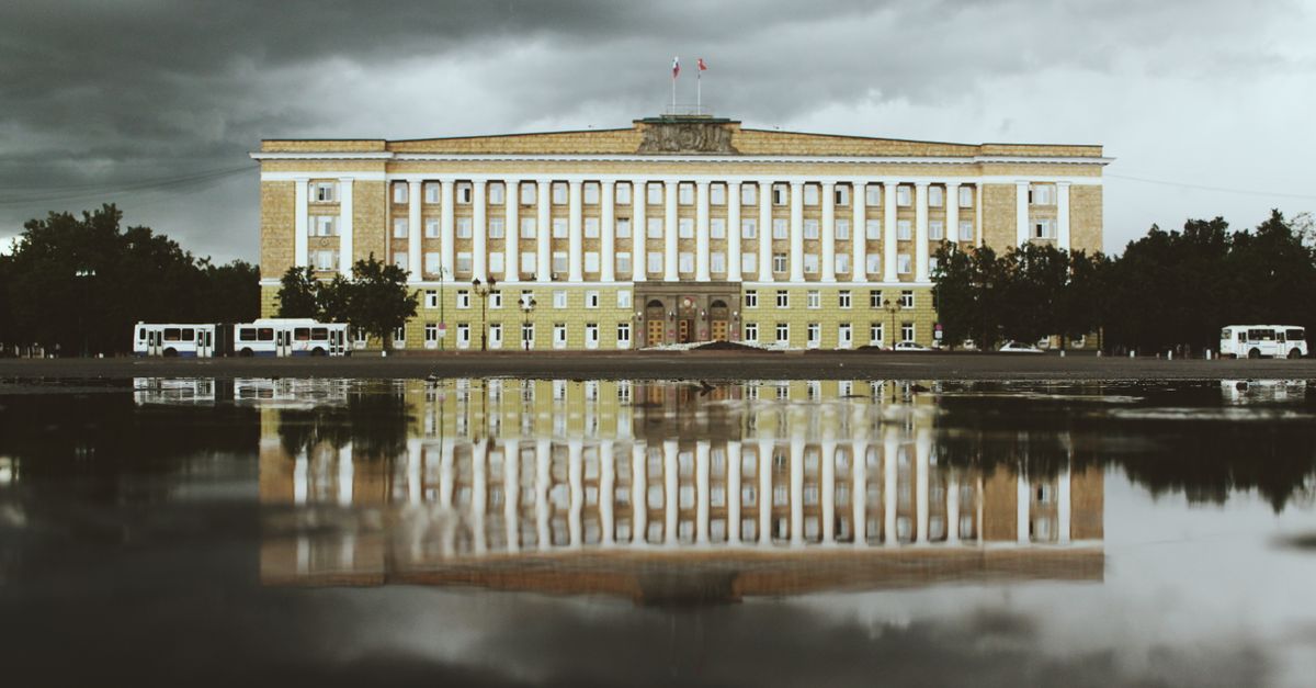 A historic building reflected in water under dramatic clouds in Veliky Novgorod, Russia.