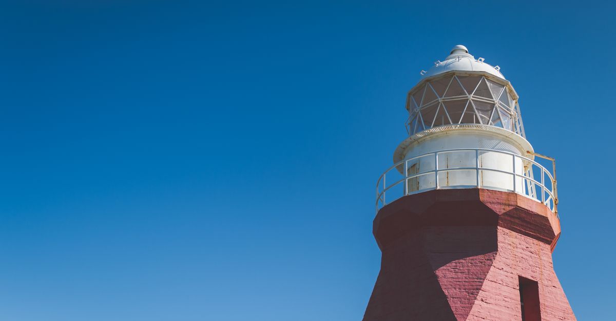 Elegant red brick lighthouse against a vivid blue sky, showcasing classic maritime architecture.