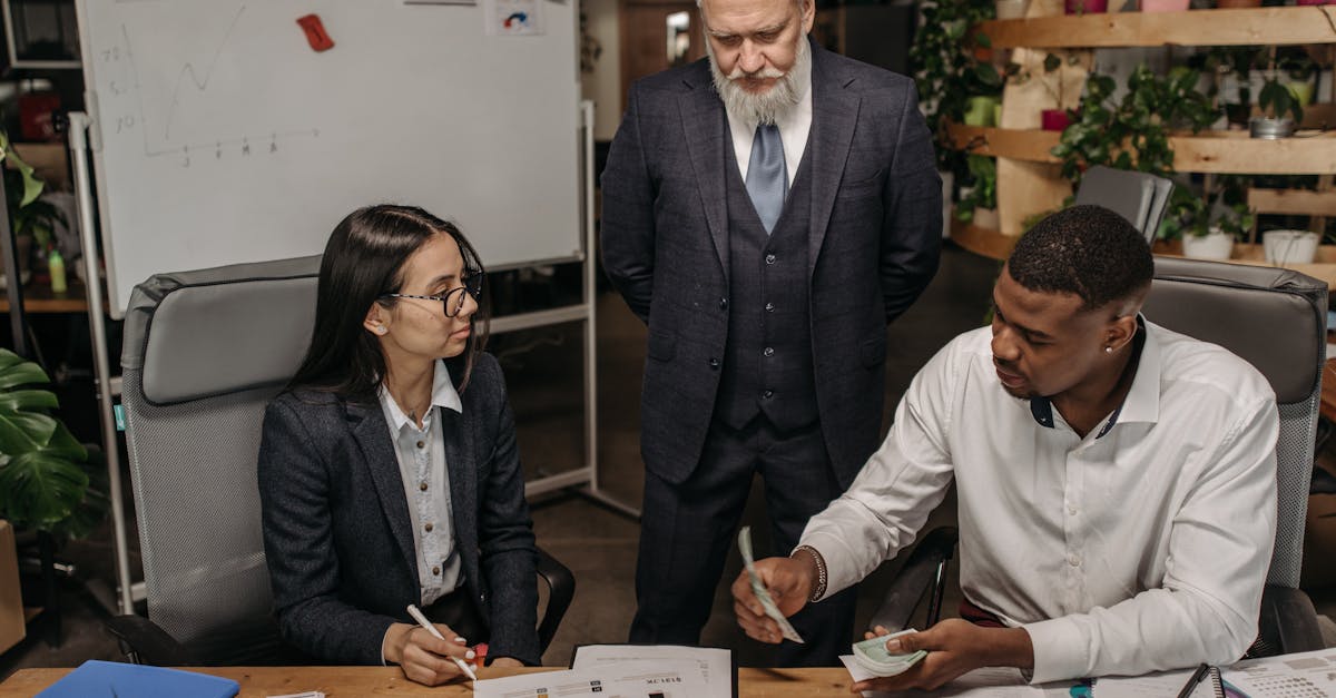 Three business professionals discussing reports at an office desk.