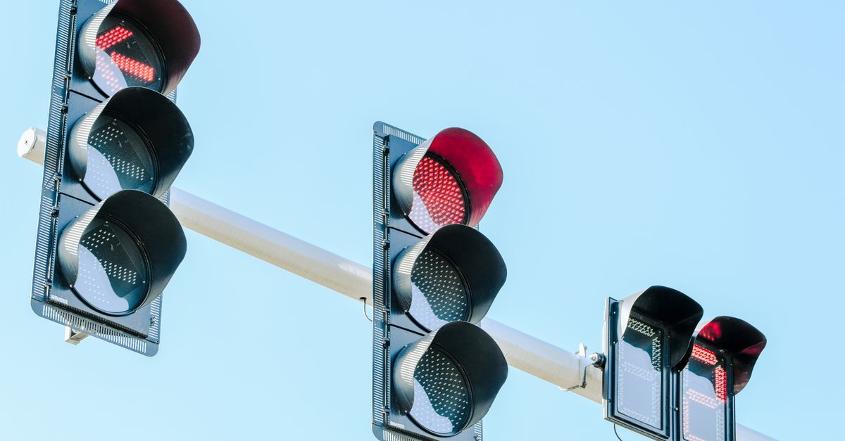 Traffic lights showing red against a clear blue sky on a sunny day.