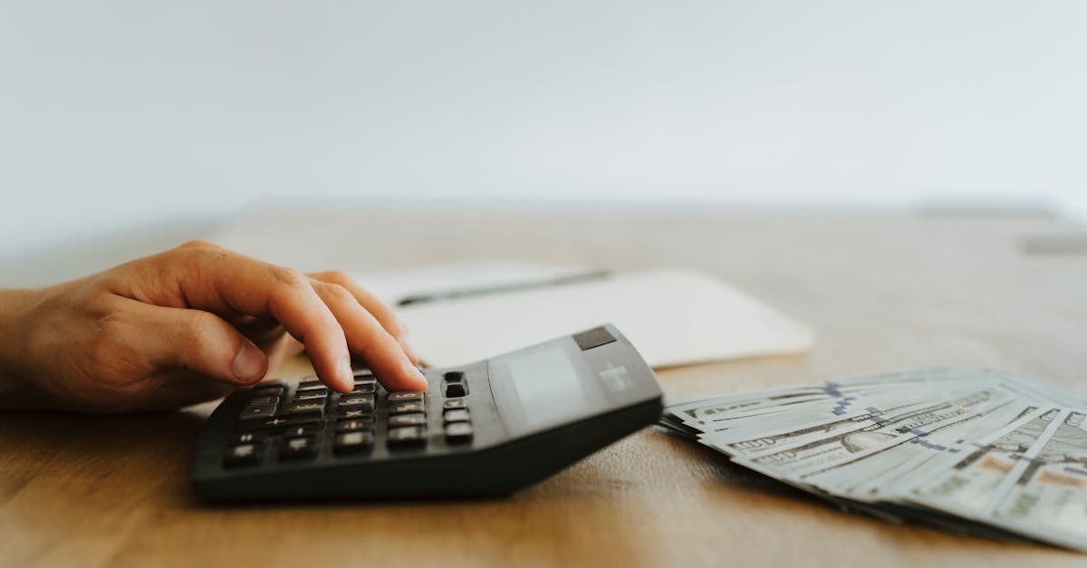 A hand calculating finances with a calculator next to stacks of US dollar bills.
