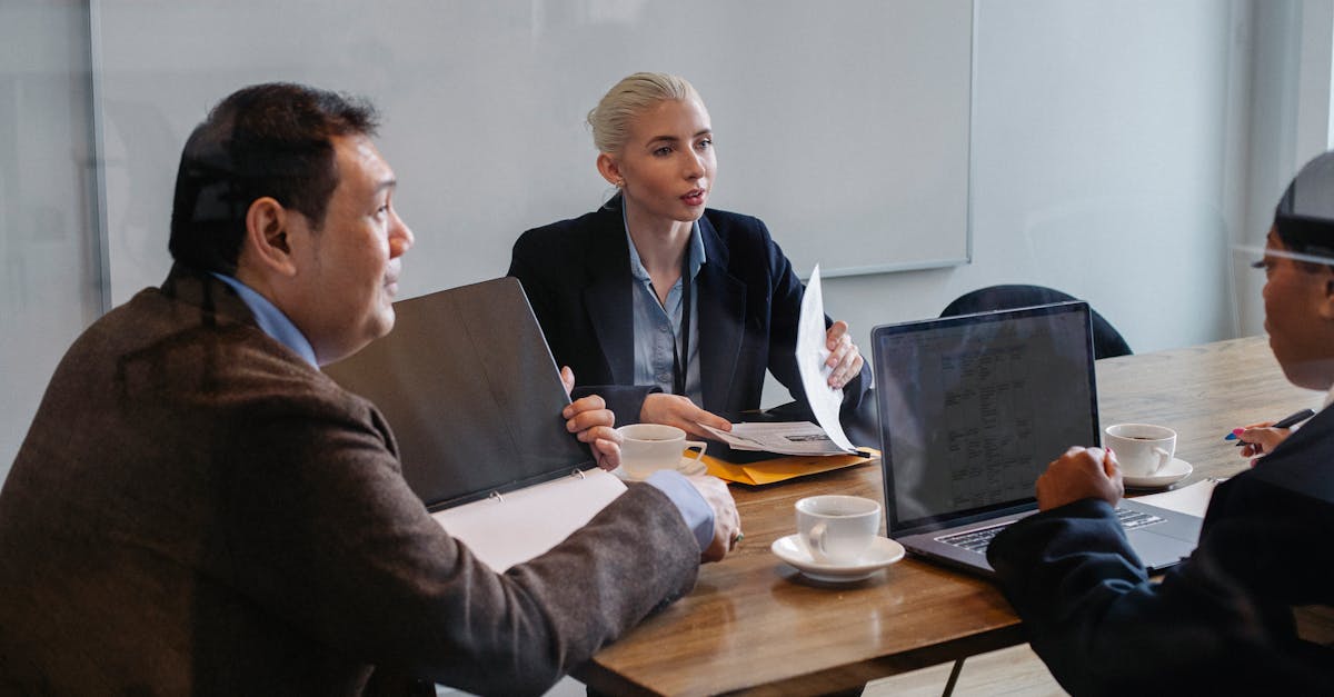 Multiracial colleagues in formal clothes sitting at table with laptop and documents while discussing details of business plan