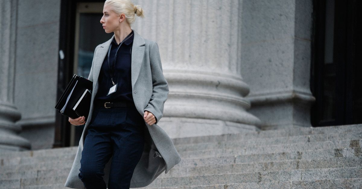 Serious female lawyer in elegant outfit holding folders with documents while going downstairs near stone state building and looking away