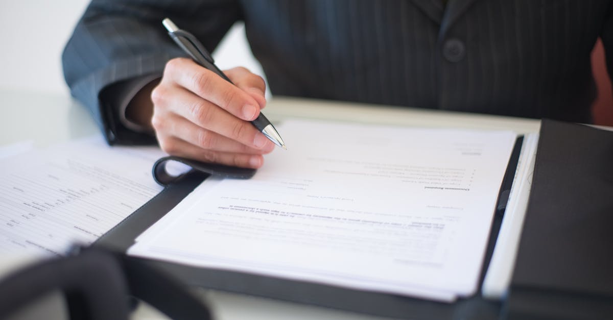 Close-up of a hand signing documents with a pen, symbolizing an important business contract.