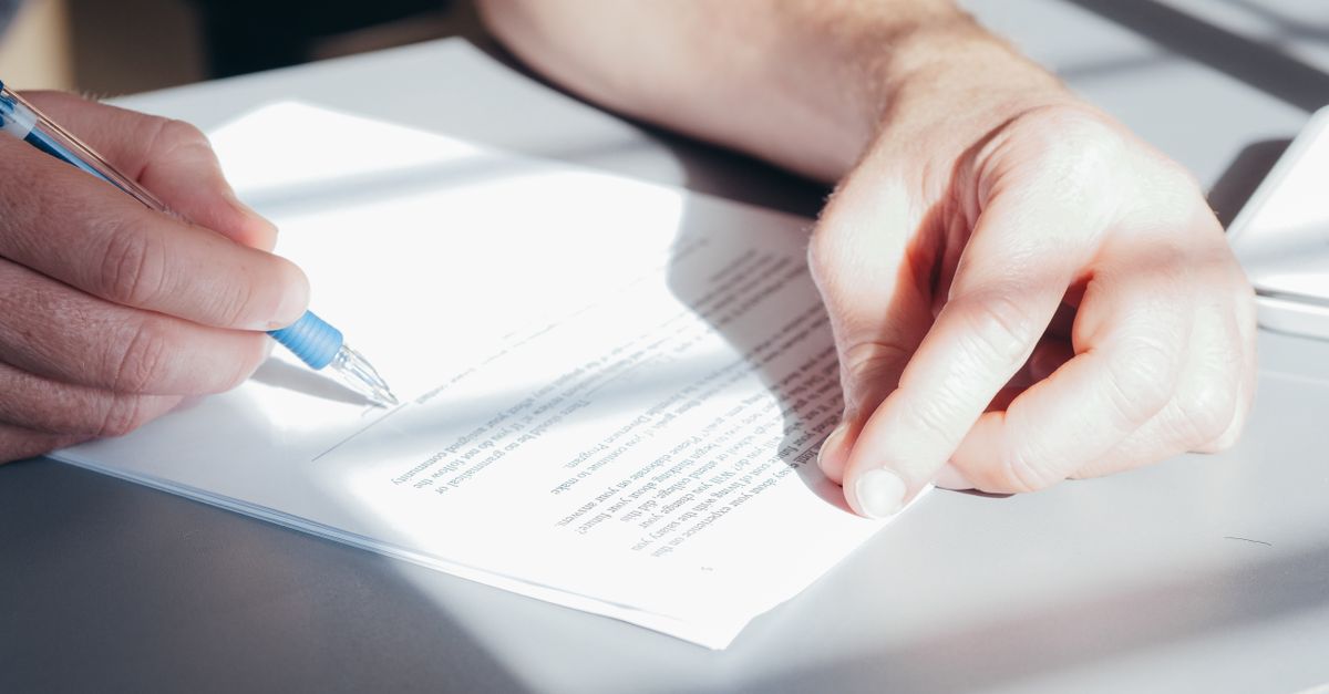 Hands signing a contract with a blue pen, close-up view.