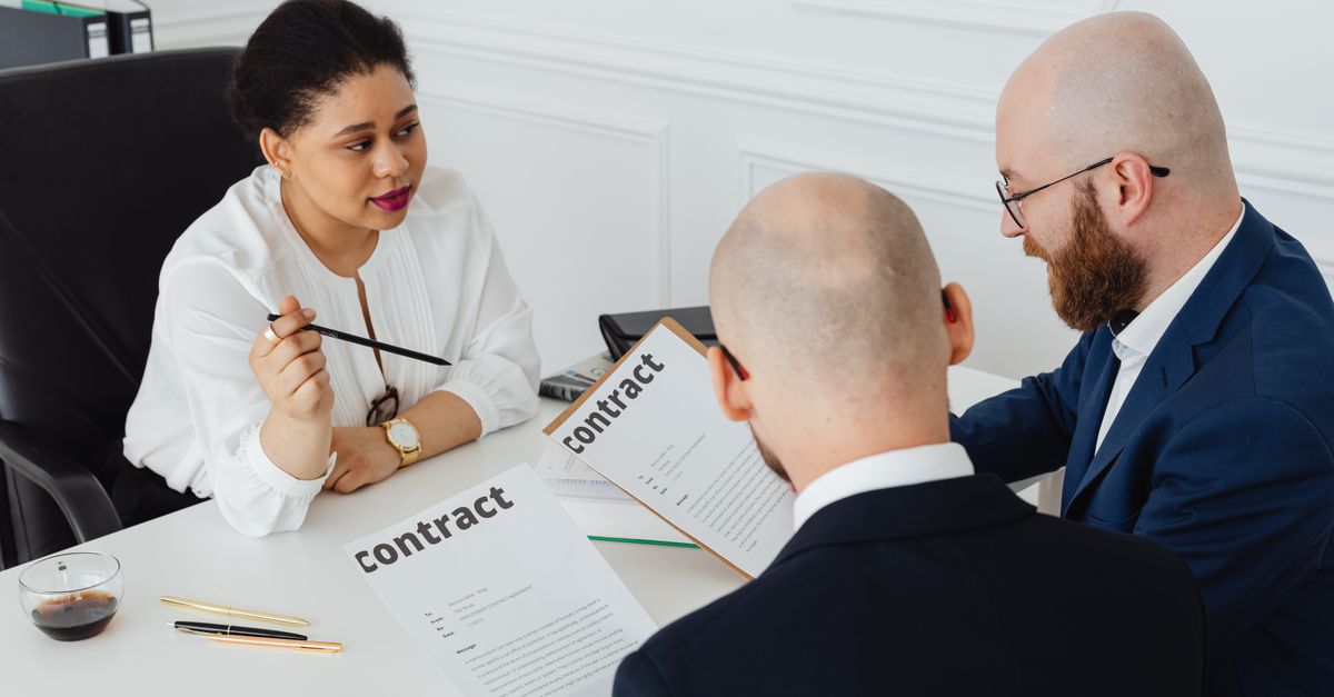 Three business professionals in discussion over a contract in a modern office setting.