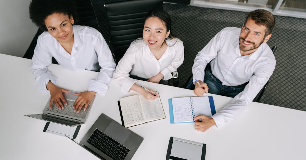 A diverse group of professionals collaborating during an office meeting, using laptops and notebooks.