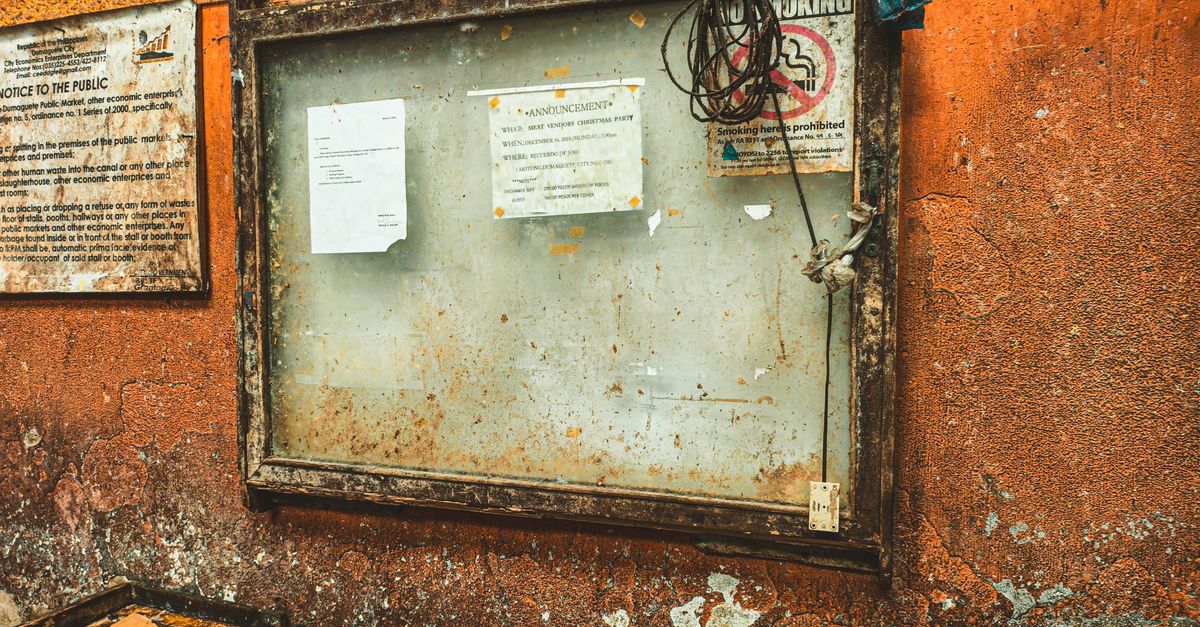 A rustic notice board with announcements on a textured orange wall in Dumaguete City, Philippines.