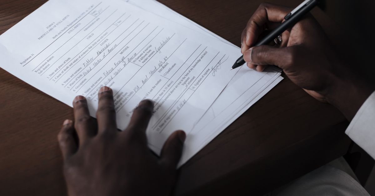 A detailed view of a man signing official documents with a pen at a table.