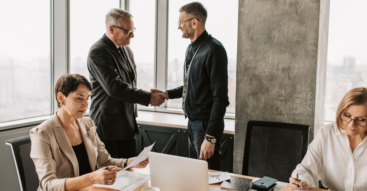 Professional business meeting with handshake in modern office room with multiple colleagues.