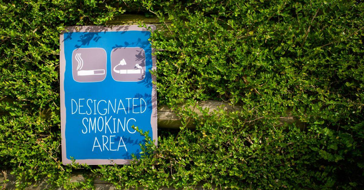 Blue designated smoking area sign surrounded by lush greenery outdoors during the day.