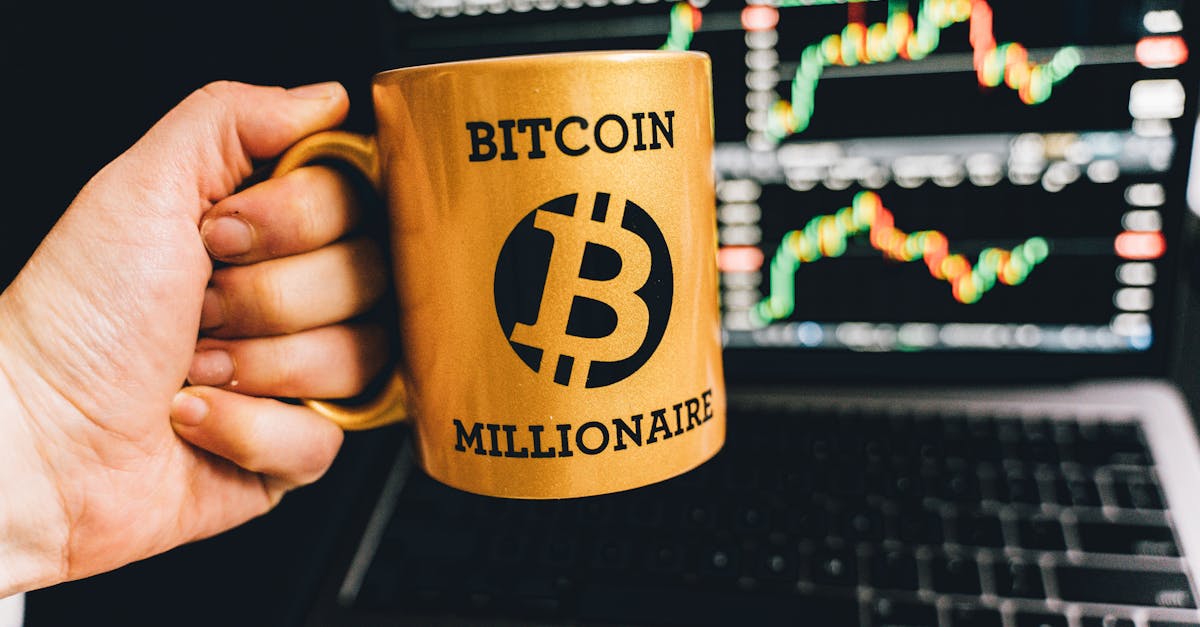 Golden mug with 'Bitcoin Millionaire' text in front of stock market charts on laptop screen.