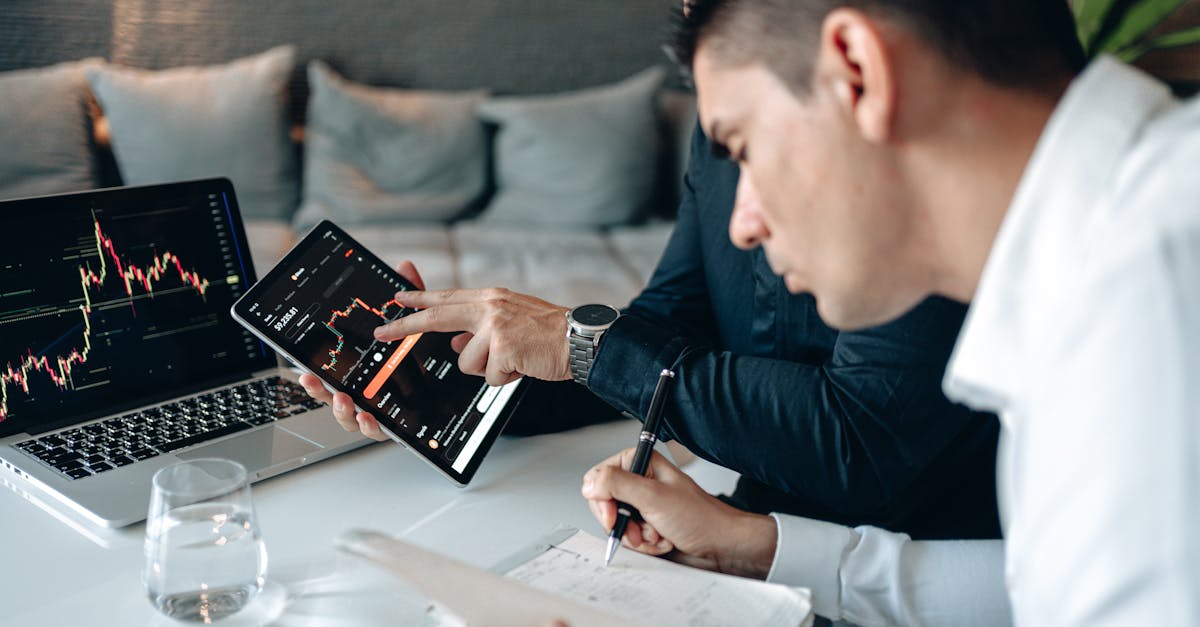 Two businessmen in a meeting analyzing financial data with digital devices and taking notes.