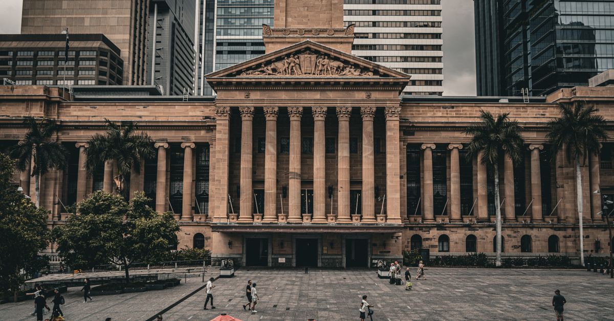 A view of Brisbane City Hall with urban surroundings and pedestrians in the plaza.