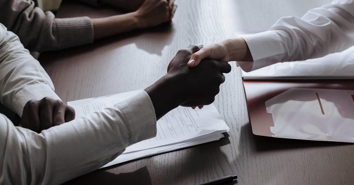 Business agreement with a handshake over contract documents at a meeting table.