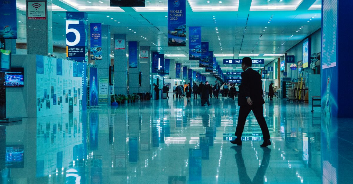An indoor view of a busy conference hall during World Summit 2020 with directional signs and reflections.