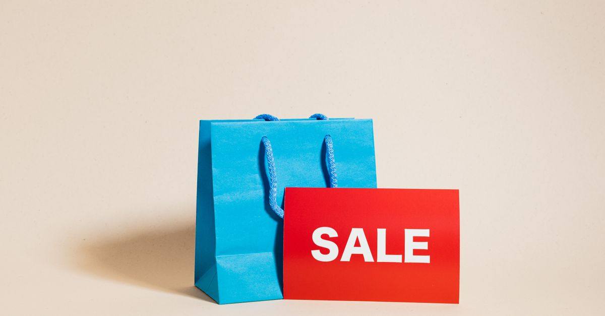 Blue shopping bag with red sale sign on neutral background, ideal for promotions.