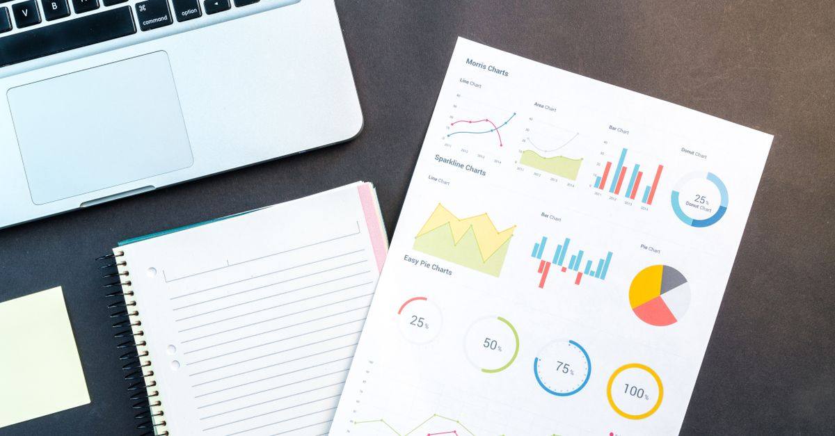 Flatlay of business report with colorful charts, a notebook, and a laptop for data analysis on a desk.