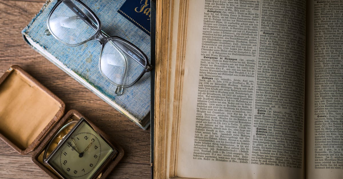 A vintage setting with antique books, watch, and reading glasses on a wooden table.
