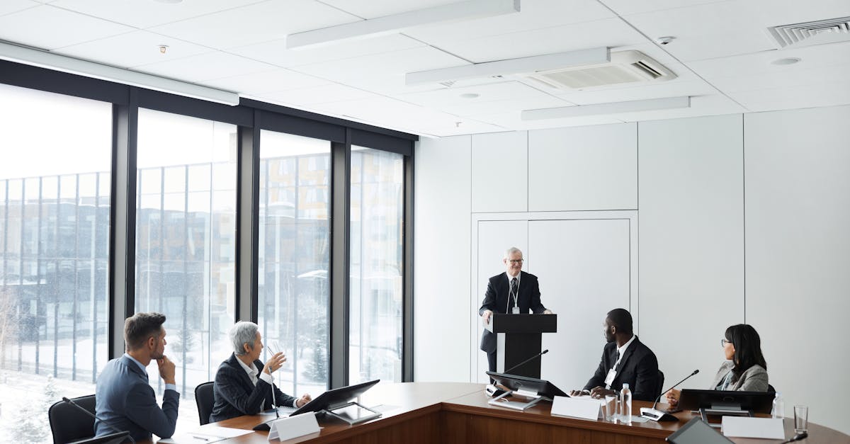 Corporate meeting with diverse professionals listening to a speaker at a podium in a modern conference room.